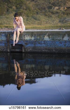 A woman sitting on a stone wall by water View Large Photo Image Stock Image - A woman sitting on a stone wall by water. Fotosearch