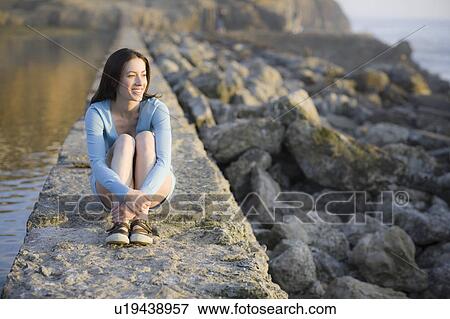 A woman sitting on a stone wall by water View Large Photo Image Stock Photo - A woman sitting on a stone wall by water. Fotosearch