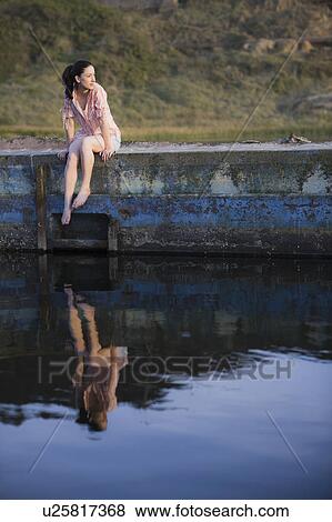 A woman sitting on a stone wall by water View Large Photo Image Stock Photo - A woman sitting on a stone wall by water. Fotosearch