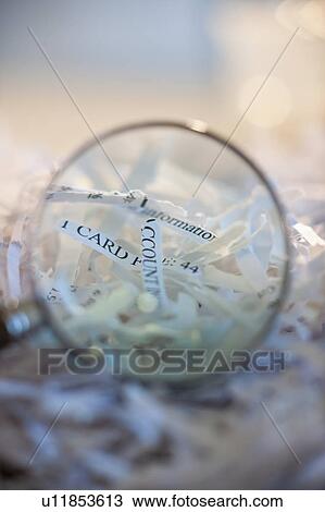 Stock Image - Confidential paperwork shredded under a magnifying glass. Fotosearch