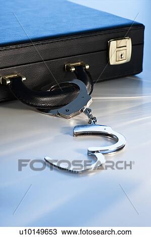Stock Image - Hand cuffs attached to a suitcase. Fotosearch