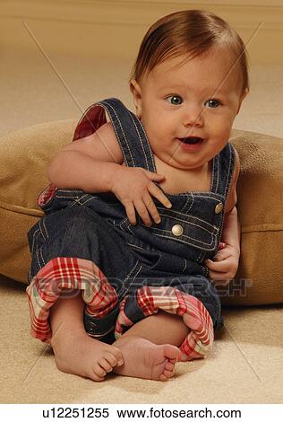 Stock Photography - Baby reclining in overalls. Fotosearch