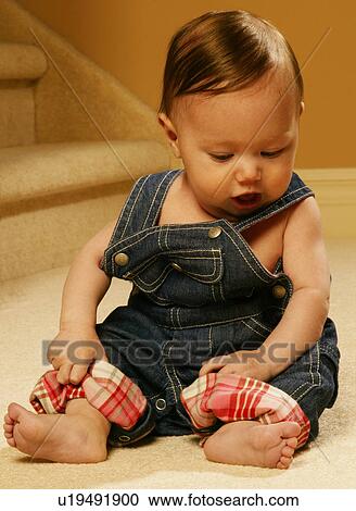 Stock Image - Baby sitting in overalls. Fotosearch