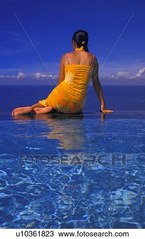 Stock Image - Back of woman sitting on edge of pool. Fotosearch