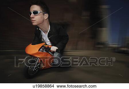 Picture - Bizarre image of man riding on a mini motorcycle. Fotosearch