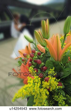 Stock Image - Bouquet of flowers with bride and groom kissing in the background. Fotosearch