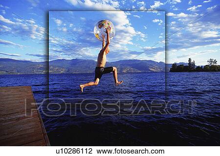 Stock Image - Boy jumping into lake with globe beach ball. Fotosearch