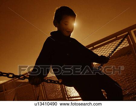 Stock Image - Boy sitting on chain link. Fotosearch