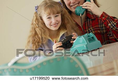 Stock Image - Child holds camera while mother on phone. Fotosearch