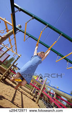 Stock Image - Child swinging on Monkey bars at playground. Fotosearch