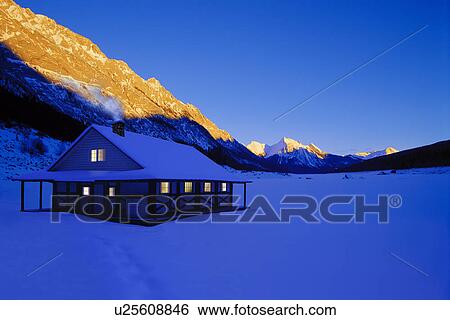 Stock Photograph - Cottage in heavy snowfall with sunrise on mountain in background. Fotosearch