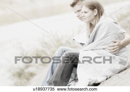Stock Photography - Couple sitting on beach with blanket. Fotosearch