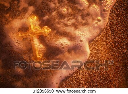 Stock Image - Cross being washed over by wave on sandy beach. Fotosearch