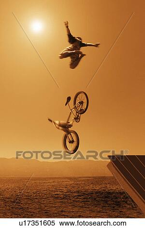 Stock Photography - Cyclist going off jump into water in brown tones. Fotosearch