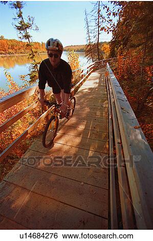 Stock Photograph - Cyclist on wooden pathway by river. Fotosearch