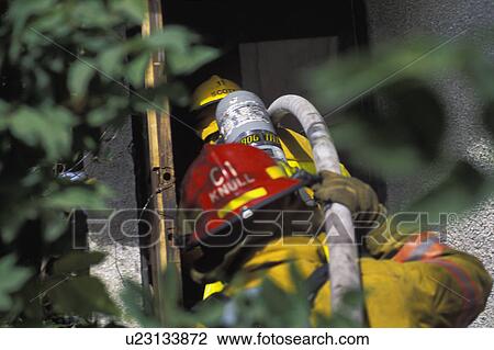 Stock Image - Fireman pulling hose to building. Fotosearch