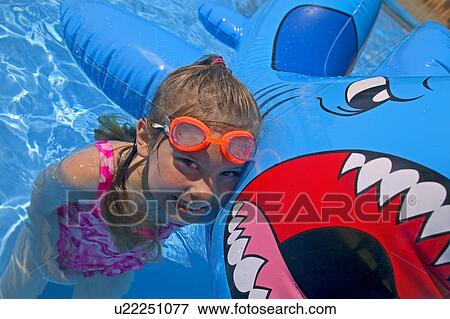 Stock Photo - Girl playing in swimming pool with inflatable shark. Fotosearch