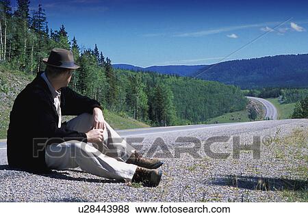 Stock Photo - Hiker sitting on edge of country road. Fotosearch
