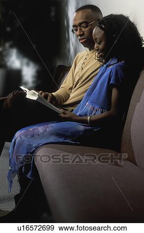 Stock Photo - Man and girl reading book on couch. Fotosearch