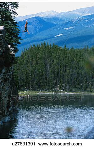 Man jumping off cliff into lake View Large Photo Image Stock Image - Man jumping off cliff into lake. Fotosearch