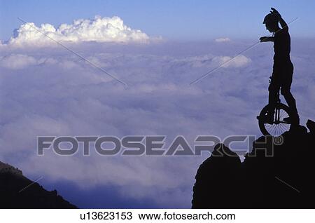 Stock Image - Man on cliff riding unicycle. Fotosearch