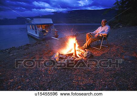 Man on shore relaxing at campfire View Large Photo Image Stock Photograph - Man on shore relaxing at campfire. Fotosearch