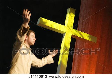 Stock Image - Man worshipping beside cross. Fotosearch