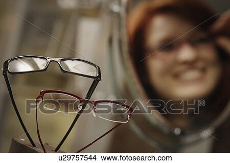 Optician's window display with woman trying on glasses in mirror in background View Large Photo Image Picture - Optician's window display with woman trying on glasses in mirror in background. Fotosearch