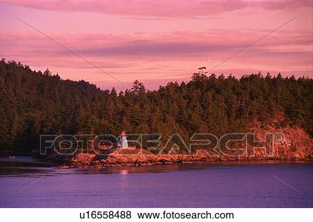 Stock Photo - Small lighthouse with trees and hill behind. Fotosearch