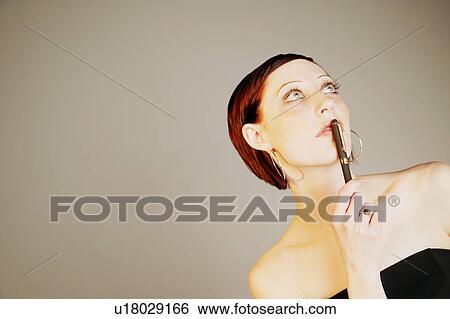 Stock Photograph - Woman holding pen to mouth. Fotosearch