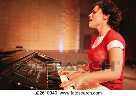 Stock Image - Woman plays the piano and sings. Fotosearch