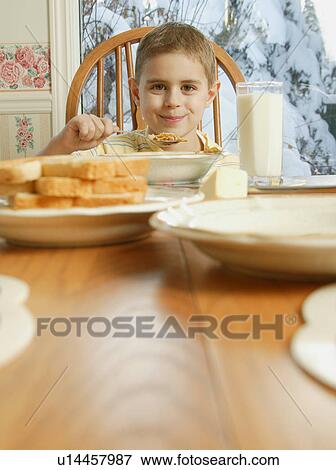 Stock Photo - Young boy eating cereal at breakfast table. Fotosearch