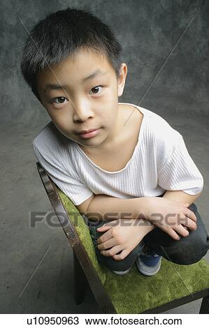 Young boy perched on chair View Large Photo Image Stock Image - Young boy perched on chair. Fotosearch