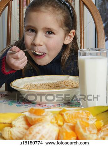 Picture - Young girl eating cereal at breakfast table. Fotosearch