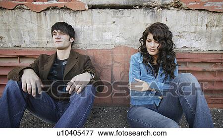 Stock Photo - Young trendy couple sitting on the sidewalk. Fotosearch
