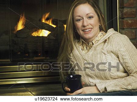 Picture - Young woman in front of fireplace. Fotosearch