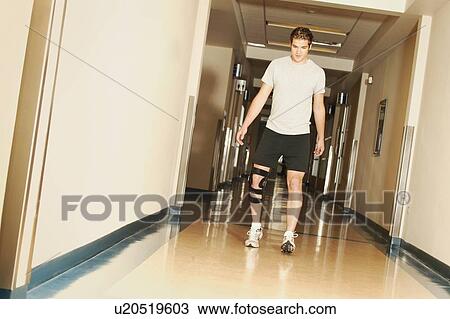 Stock Image - A young man walking with a knee brace in a hospital. Fotosearch
