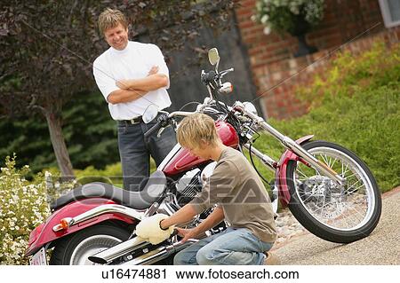Stock Image - Father watches son polish motorcycle. Fotosearch