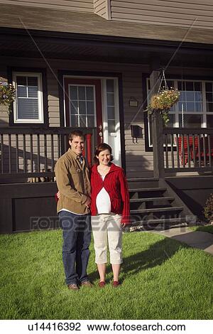 Stock Image - Couple standing in front of new house. Fotosearch