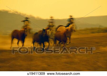 Stock Photo - Cowboys on horseback herding running horses, Ponderosa Ranch, soft focus.. Fotosearch