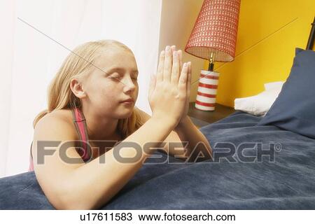 Stock Image - Child prays at her bedside. Fotosearch