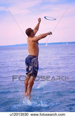 Stock Image - Man jumping for flying disc. Fotosearch
