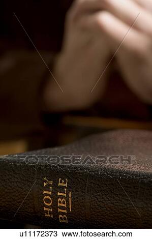 Stock Image - Closeup of Bible with praying hands. Fotosearch