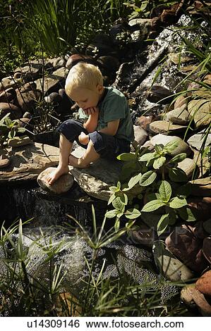 Stock Photograph - Boy sitting by pond. Fotosearch