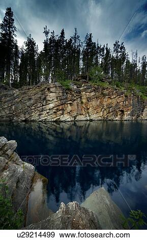 Stock Photo - Tree covered rocky hill reflected in water. Fotosearch
