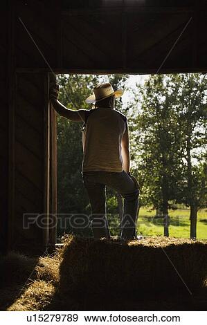 Man wearing work gloves and cowboy hat stands in barn leaning in doorway and looking out View Large Photo Image Stock Photo - Man wearing work gloves and cowboy hat stands in barn leaning in doorway and looking out. Fotosearch