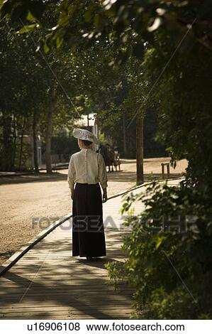 Stock Photo - Old-fashioned woman walking down board-walk street. Fotosearch