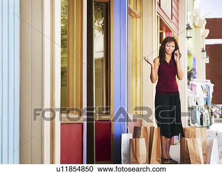 Stock Image - Woman talking on cell phone with shopping bags around her. Fotosearch
