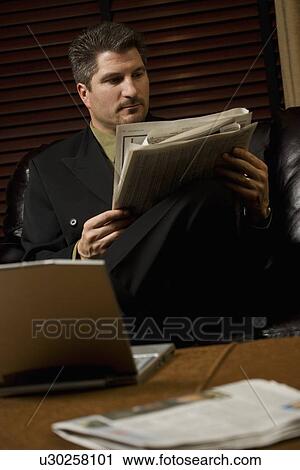 Businessman reading the newspaper with laptop View Large Photo Image Stock Image - Businessman reading the newspaper with laptop. Fotosearch