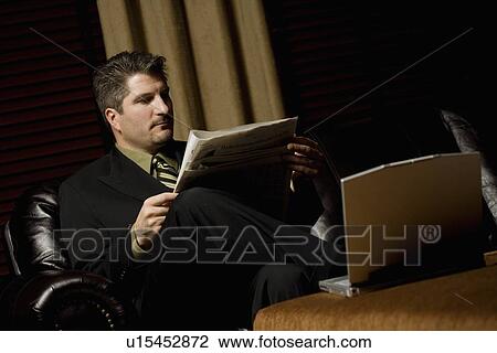 Businessman reading the paper with his laptop View Large Photo Image Stock Image - Businessman reading the paper with his laptop. Fotosearch